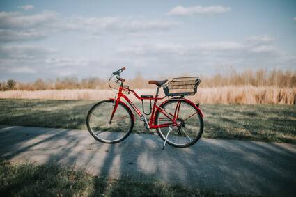 Als regionaler Immobilienmakler für Hamminkeln schätzen wir besonders die Nähe zur Natur. Das Foto zeigt daher ein rotes Fahrrad auf einem Fahrradweg vor einem Feld.